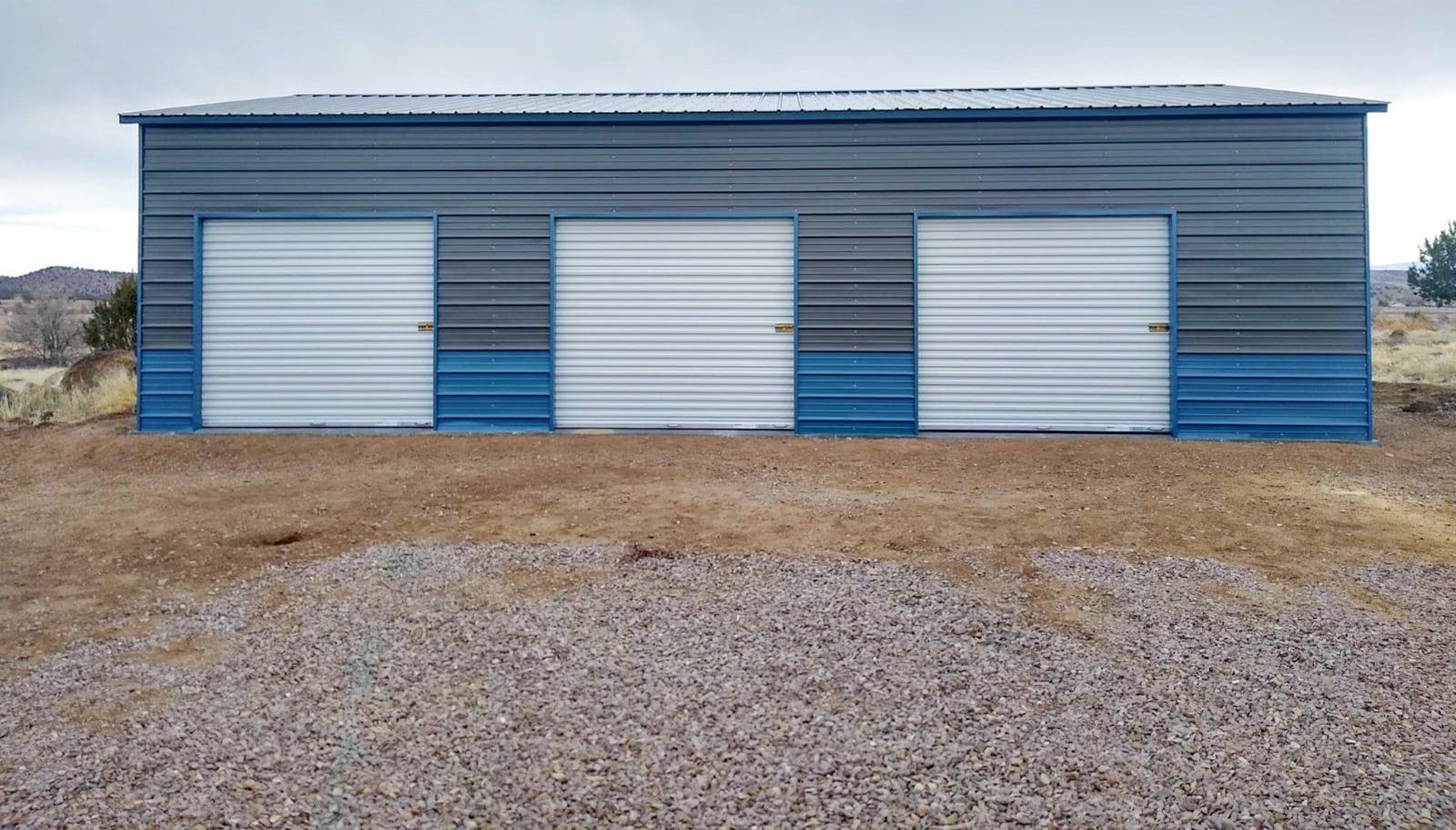 Long blue and gray steel garage with three white roll-up doors