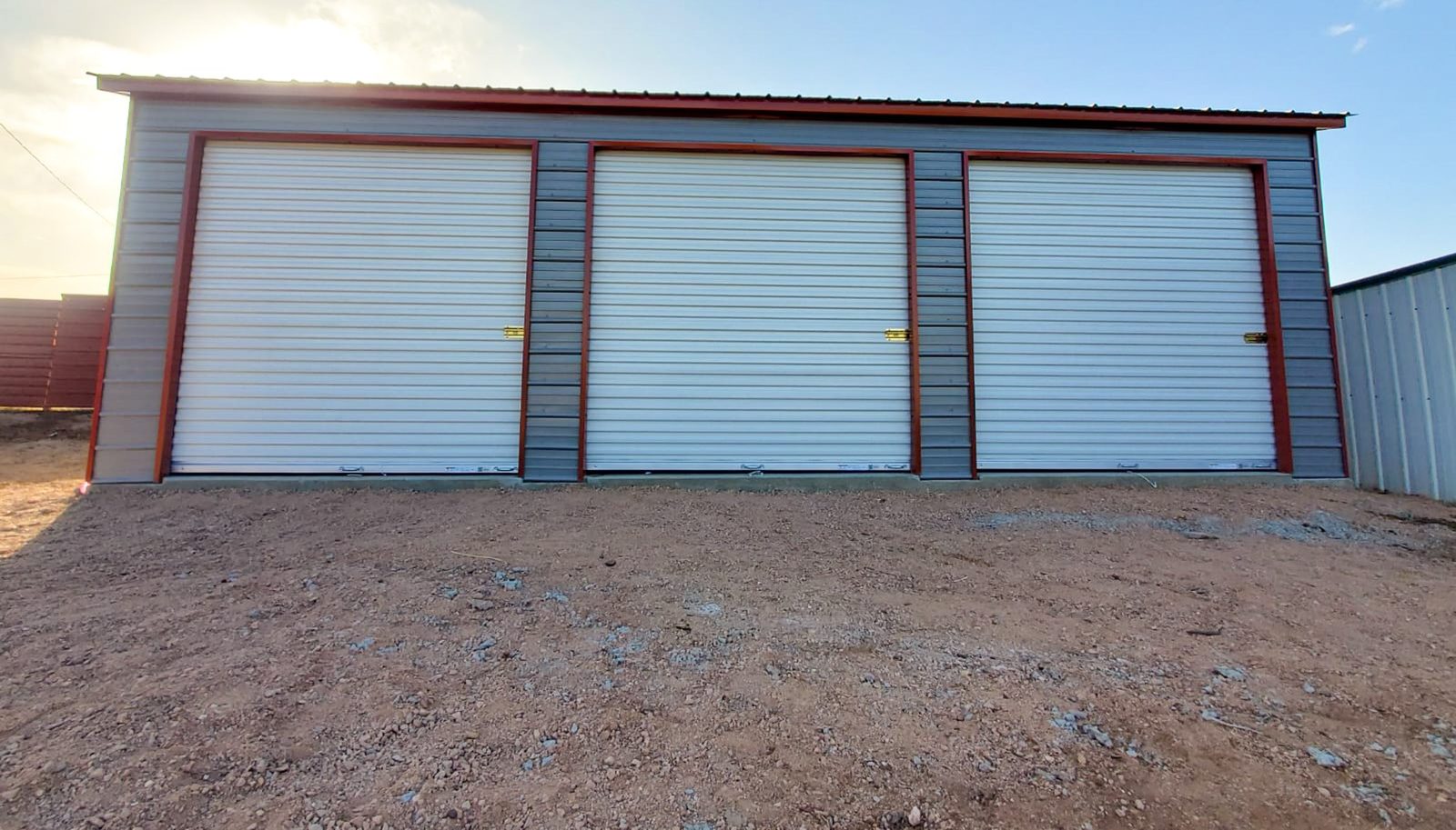 Steel garage with three white roll-up doors and red trim