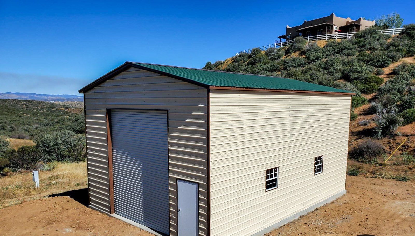 Tall tan steel workshop with green roof on hillside lot
